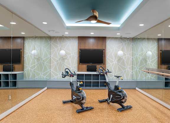 Two stationary bikes are in a room with a patterned wallpaper.