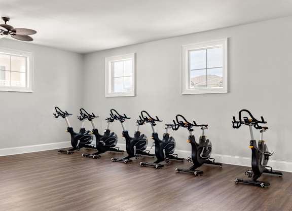 A room with a row of stationary bikes and a ceiling fan.