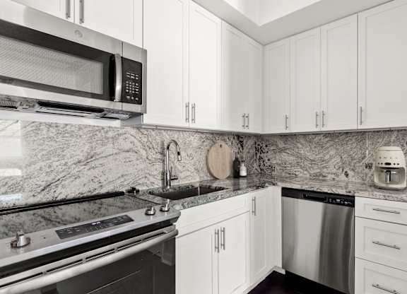 A kitchen with white cabinets and a marble backsplash.