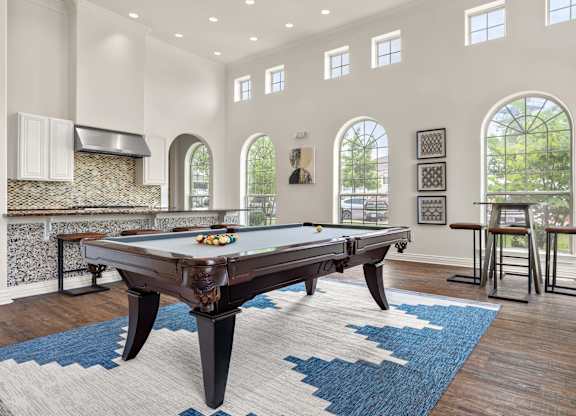 A pool table in a room with arched windows and a stone fireplace.