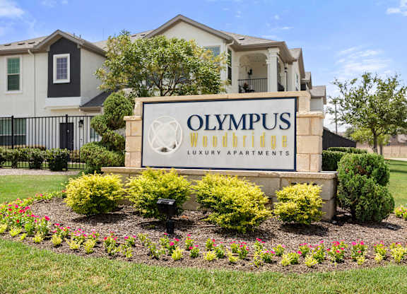 A sign for Olympus Woodbridge Luxury Apartments is in front of some buildings.
