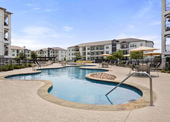 A large outdoor swimming pool surrounded by a concrete patio and chairs.