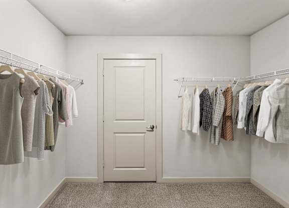 A white door is in a room with clothes hanging on the wall.