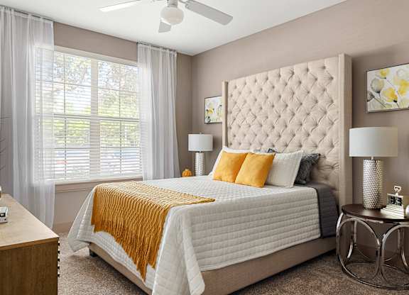 A bedroom with a large bed, a ceiling fan, and a window with white curtains.