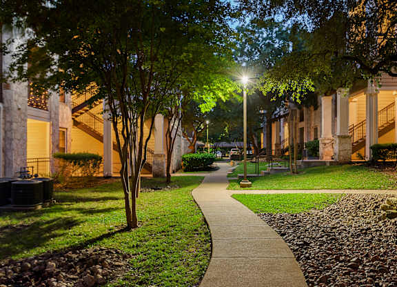 A walkway with trees and lights on the side of a building.