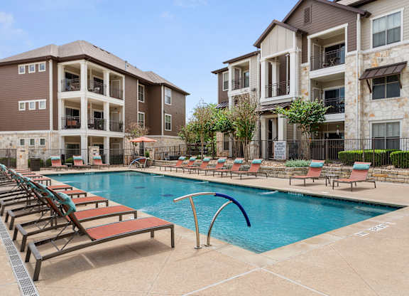 A swimming pool with lounge chairs and apartment buildings in the background.