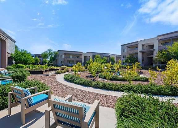 A sunny day at a residential complex with a bench and a chair in the foreground.