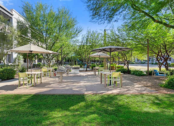 A sunny day at the park with tables and chairs under umbrellas.