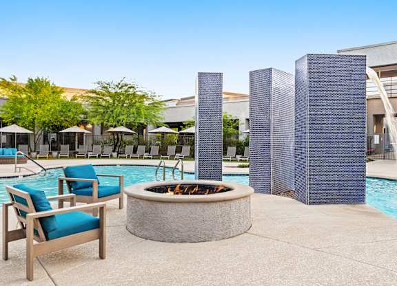 A poolside area with a fire pit, chairs, and umbrellas.