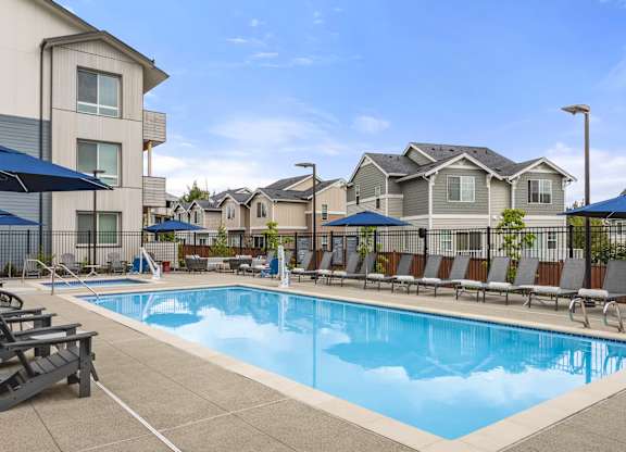 A swimming pool surrounded by lounge chairs and umbrellas in a residential area.
