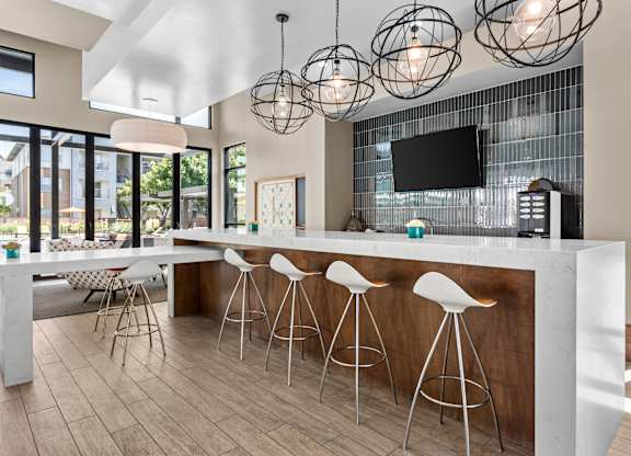 A modern kitchen with a bar area and white stools.