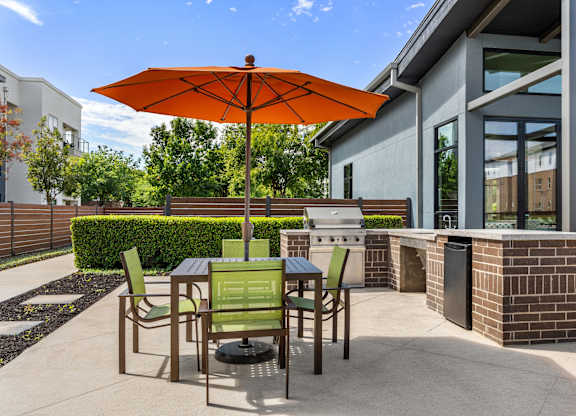 A patio with a table and chairs under an orange umbrella.