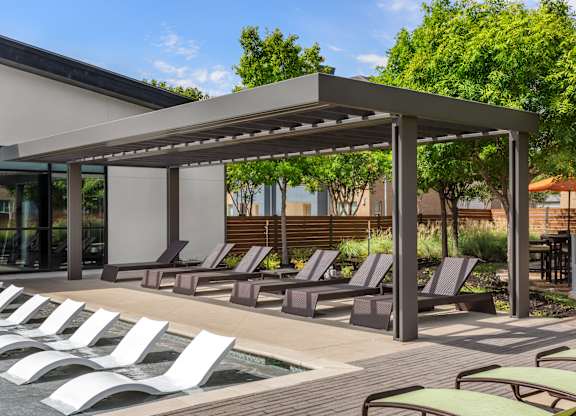A row of sun loungers are arranged on a wooden deck next to a pool.