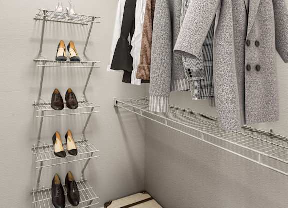 A closet with a coat hanging on a rod and a shelf with shoes.
