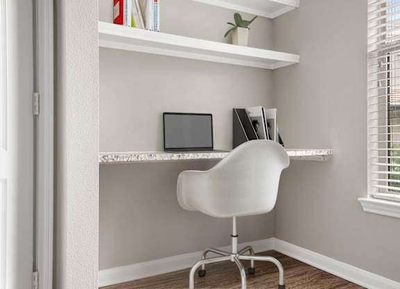 A white chair is in front of a desk with a laptop and a plant on it.