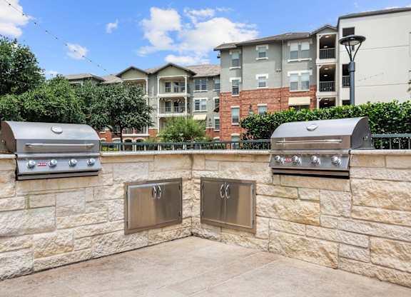 Two outdoor grills are built into a stone wall.