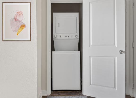 A white dishwasher is in a narrow space between a white door and a white wall.