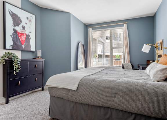 A bedroom with a large bed, a dresser, and a window with blinds.