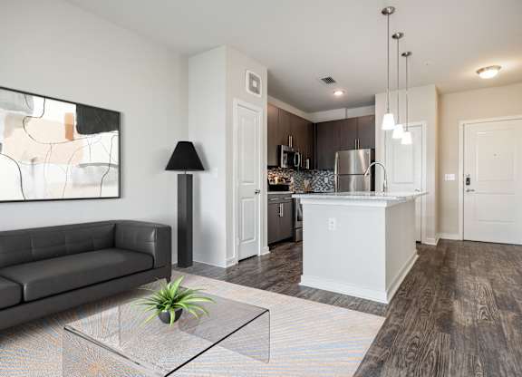 A modern living room with a black couch, a glass coffee table, and a plant on it.