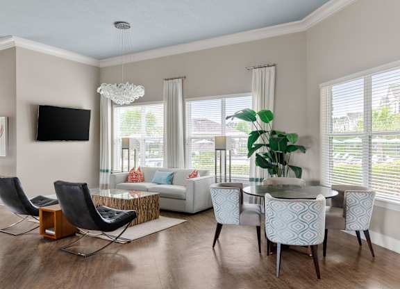 A modern living room with a white sofa, a glass coffee table, and a TV mounted on the wall.