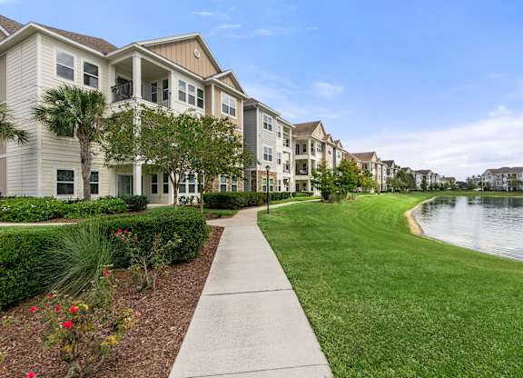 A row of houses with a sidewalk and a lake in front.