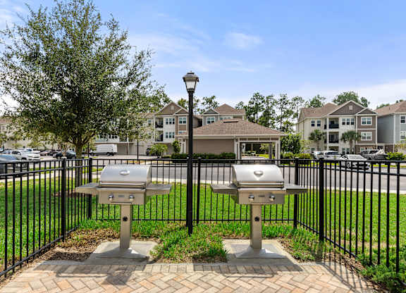 Two grills are in front of a black fence.