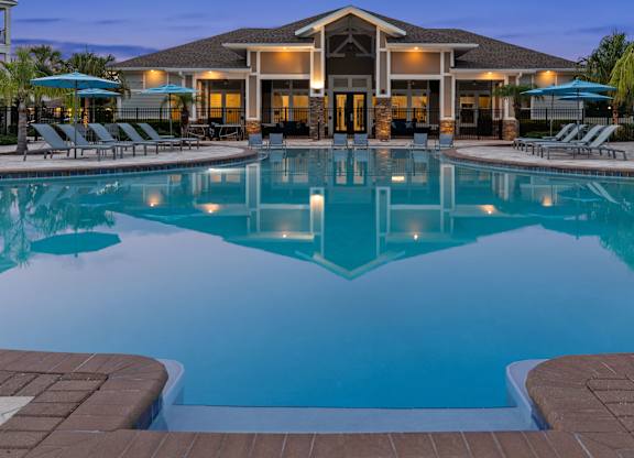 A large swimming pool in front of a building with lounge chairs and umbrellas.