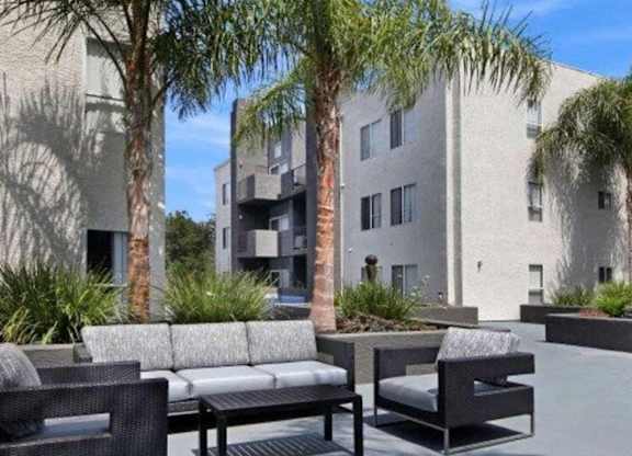 A patio with furniture and palm trees in front of a building.