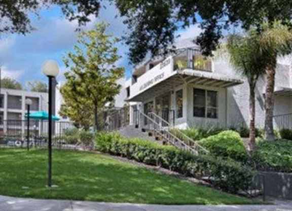 A white building with a green awning is surrounded by trees and bushes.