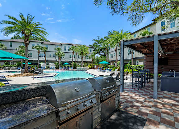 A BBQ grill is in the foreground of a resort style pool area.