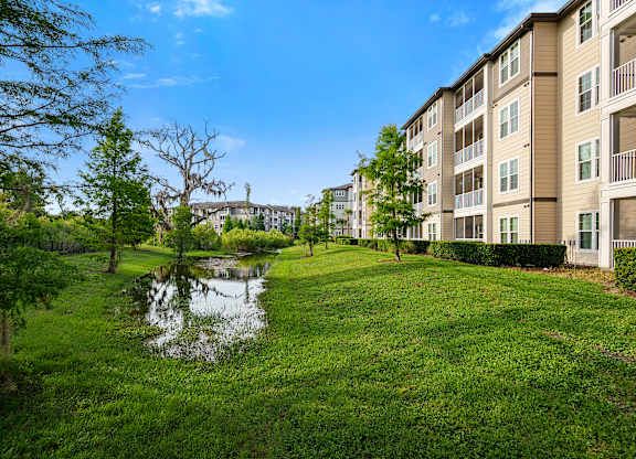 A pond in a grassy area in front of apartment buildings.