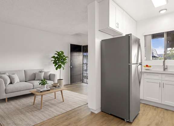 A modern kitchen with a grey refrigerator and a grey sofa with a wooden coffee table in front of it.