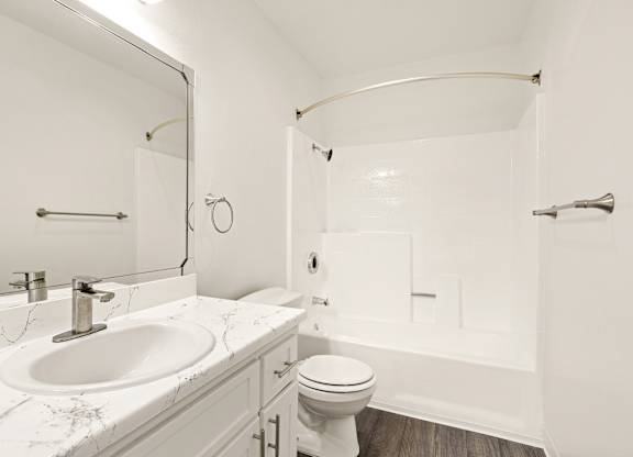 A white bathroom with a marble counter top and a white toilet.