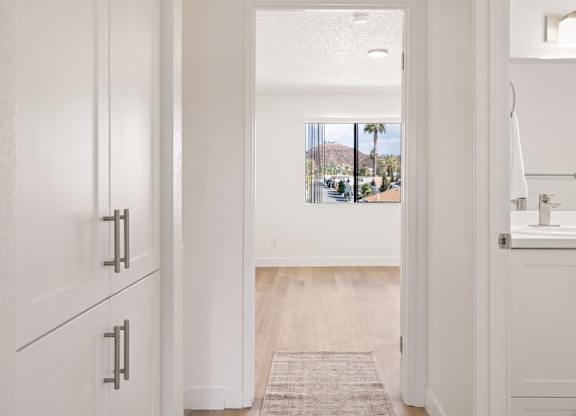 A white doorway leads to a bathroom with a sink and a window.