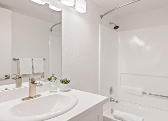 A white bathroom with a sink, mirror, and shower.