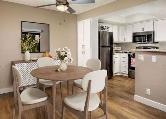 A dining room with a table and chairs and a kitchen in the background.