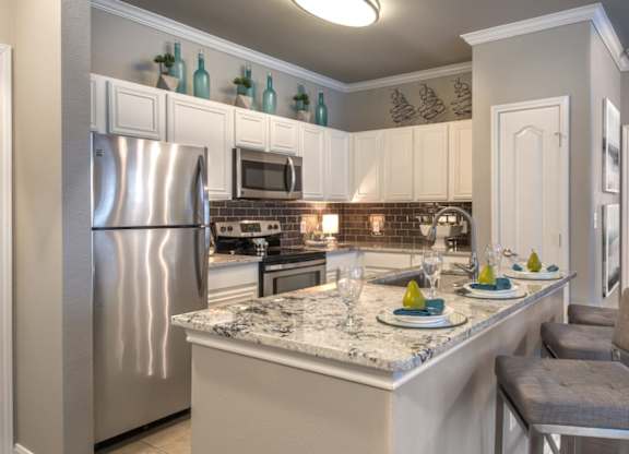 A kitchen with a marble countertop and a stainless steel refrigerator.