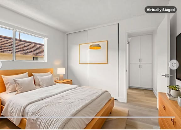 A bedroom with a large bed, a nightstand with a lamp, and a TV on the wall.