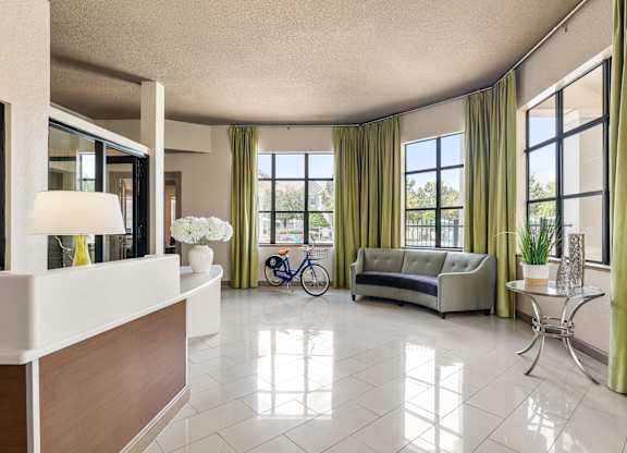 A well-lit, spacious living room with a white reception desk and a bicycle in the background.