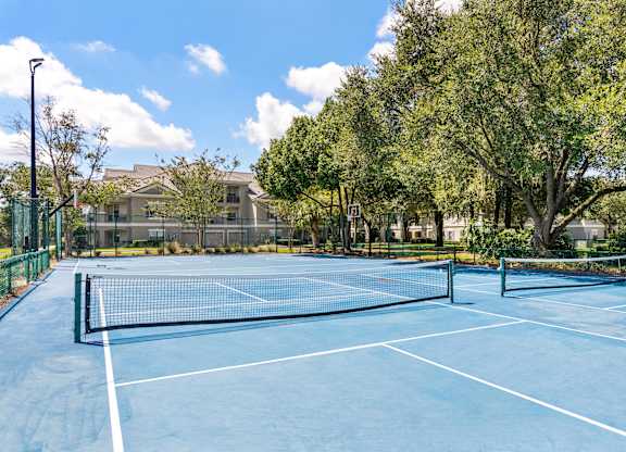 A tennis court surrounded by trees and a building in the background.