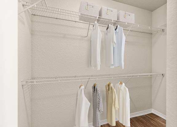 A white closet with clothes hanging on hangers.