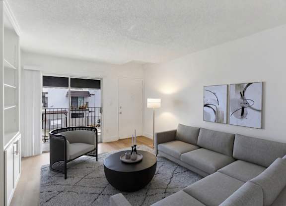 A living room with a grey couch, a black chair, and a table with a lamp on it.