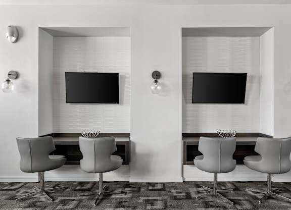 Two chairs are placed in front of two TVs on a wall.