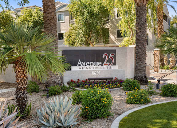 A sign for Avenue 25 Apartments is surrounded by plants and trees.