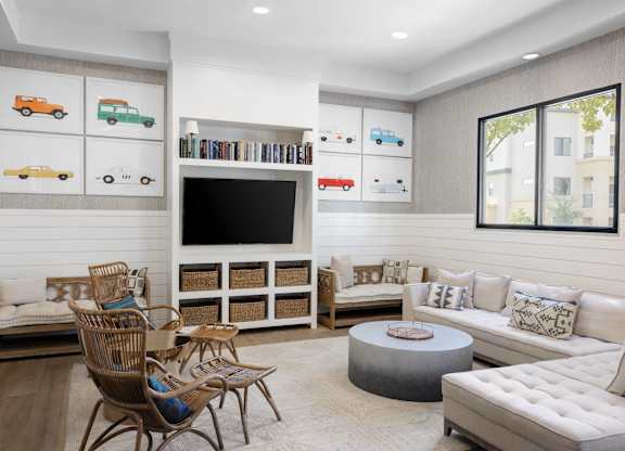 A living room with a white couch, a grey ottoman, a wooden coffee table, and a television.