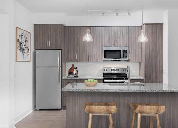A modern kitchen with a refrigerator, microwave, oven, and a counter with two chairs.