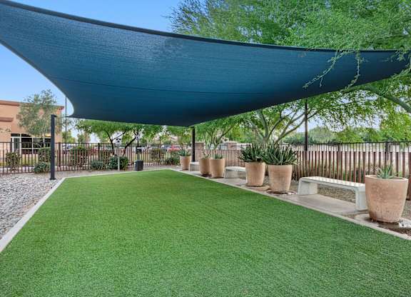 A patio with a blue shade sail and artificial grass.