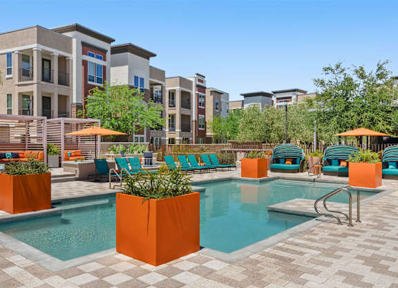 A pool surrounded by orange planters and chairs.