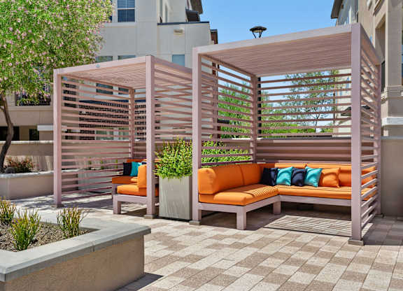 A wooden bench with orange cushions is situated under a wooden trellis.
