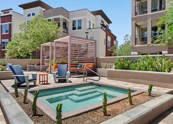 A pool surrounded by a patio with chairs and a table.